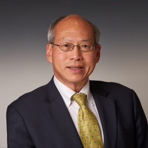 A man with glasses wearing a navy suit jacket and yellow tie.