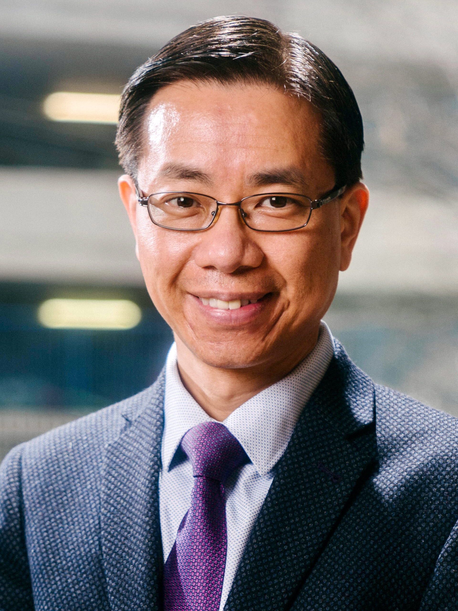 A man with glasses wearing a navy suit jacket and yellow tie.